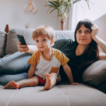 a woman and a child sitting on a couch looking at a cell phone — Foto por Helena Lopes na Unsplash