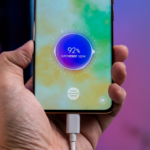 a person holding a cell phone with a charger in their hand — Foto por Amanz na Unsplash